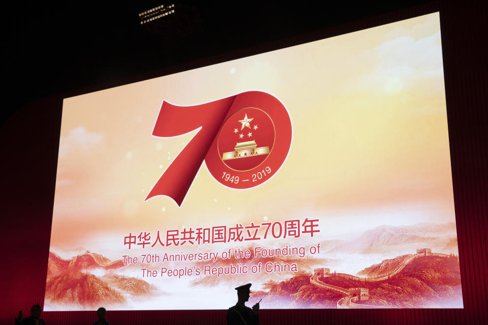 In this Saturday, Sept. 28, 2019, photo, a Chinese paramilitary policeman is silhouetted by a display showing the upcoming 70th anniversary of the Founding of the People's Republic of China in Beijing. Chinese President Xi Jinping has an ambitious goal for China: to achieve "national rejuvenation" as a strong and prosperous nation by 2049, which would be the 100th anniversary of Communist Party rule. One problem: U.S. President Donald Trump wants to make the United States great again too. (AP Photo/Ng Han Guan)