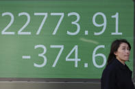 A woman walks by an electronic stock board of a securities firm in Tokyo, Thursday, Nov. 21, 2019. Shares skidded Thursday in Asia after moderate declines on Wall Street as anxious mounted over the possibility the U.S. and China may not reach a trade deal before next year. (AP Photo/Koji Sasahara)