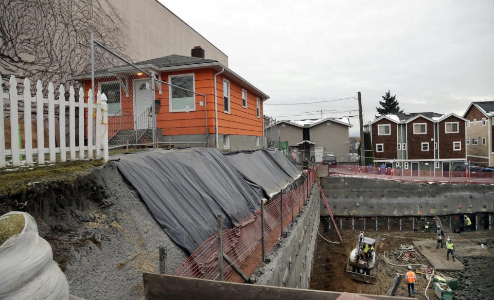 FILE - In this Dec. 27, 2017, photo, a single-family home remains on the edge of where a multi-story, mixed-use building is being constructed in Seattle. Amazon said Thursday, June 23, 2022, it will provide $23 million to help minority-led organizations build or preserve more than 500 new affordable housing units in Seattle — the latest spending by a tech company to ease a severe housing crunch the industry has helped create. (AP Photo/Elaine Thompson, File)