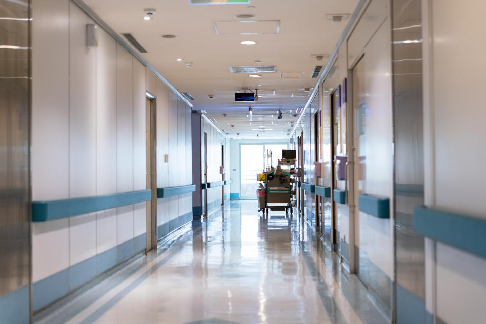 Reflection on flooring in empty corridor. Medical equipment by wall. It is in hospital.