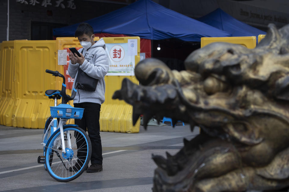 A resident wearing a mask against the coronavirus checks his phone near a sealed off community in Wuhan in central China's Hubei province on Sunday, April 5, 2020. The quarantine in the city which is the epicenter of China's coronavirus outbreak is to be formally lifted on Wednesday. (AP Photo/Ng Han Guan)