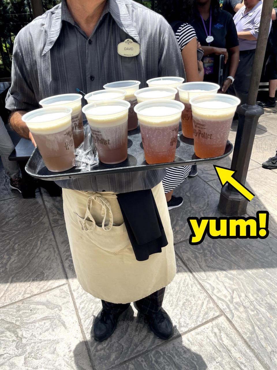 a person holding a tray of butterbeer with the word "Yum!"