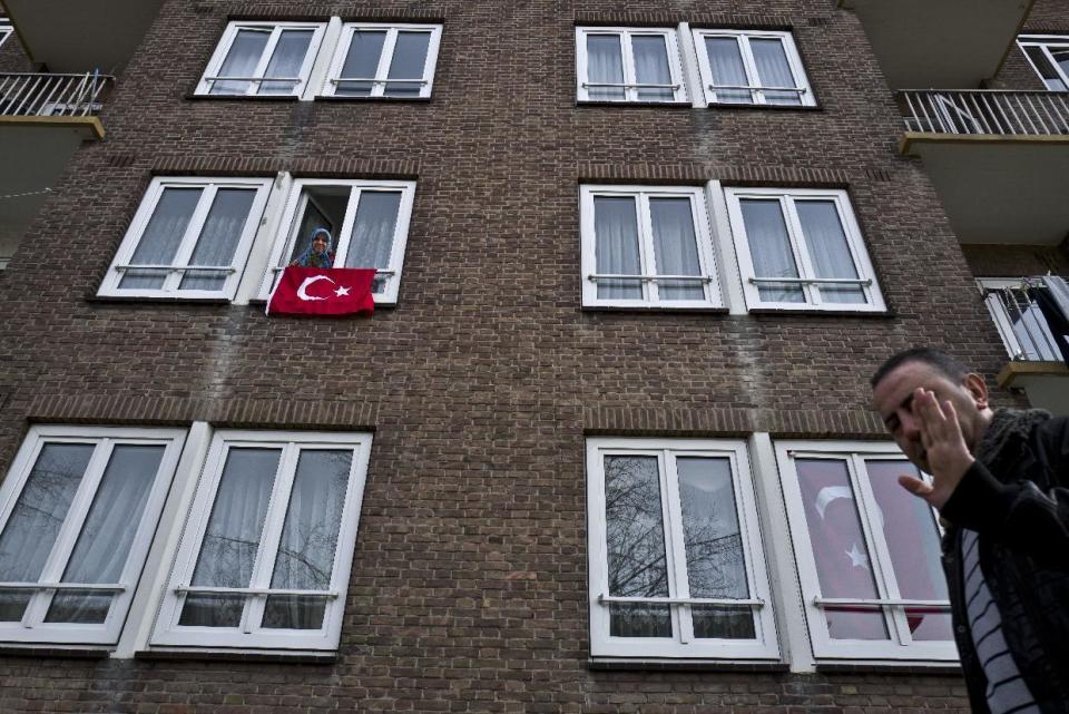 A man, right, gestures while walking by an apartment building decorated with Turkish flags in Amsterdam, Netherlands, Monday, March 13, 2017. Turkish President Recep Tayyip Erdogan says he appropriately accused the Dutch government of "Nazism and fascism," saying only those types of regimes would bar foreign ministers from traveling within their countries. Erdogan also said during a live televised address on Sunday that the Netherlands would "pay the price" for sacrificing its ties with a NATO ally to upcoming elections there. (AP Photo/Muhammed Muheisen)