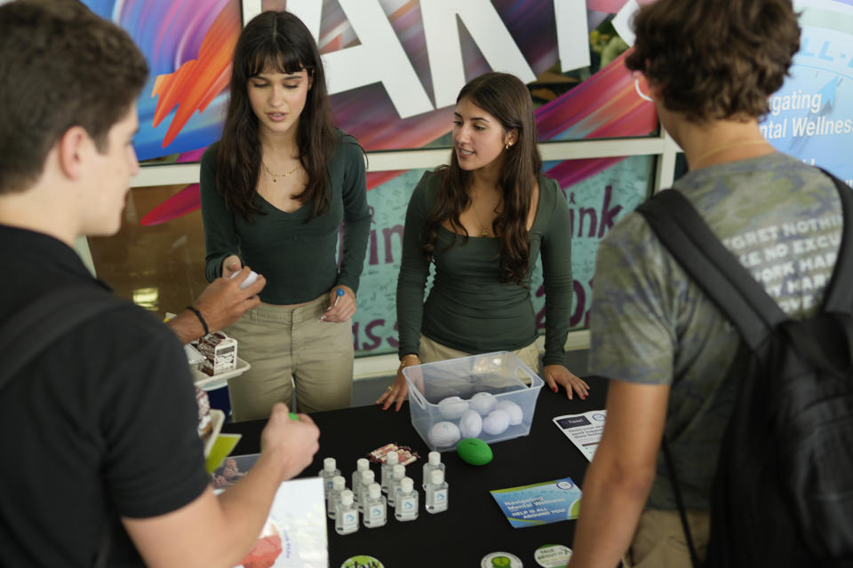 Members of the Miami Arts Studio mental health club Angelie Has, center left, and Hillary Pedrol, center right, man a table as they pass out information and stress balls to other students, on World Mental Health Day, Tuesday, Oct. 10, 2023, at the public 6th-12th grade magnet school in Miami. (AP Photo/Rebecca Blackwell)