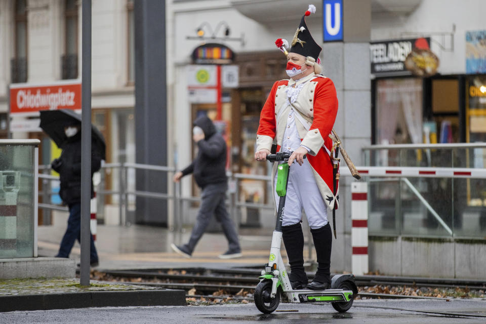 A carnival reveller rides an electric scooter near the Severinstor gate in Cologne, Germany, Monday, Feb. 15, 2021. Because of the coronavirus pandemic the traditional carnival parade in the city are canceled. (Rolf Vennenbernd/dpa via AP)