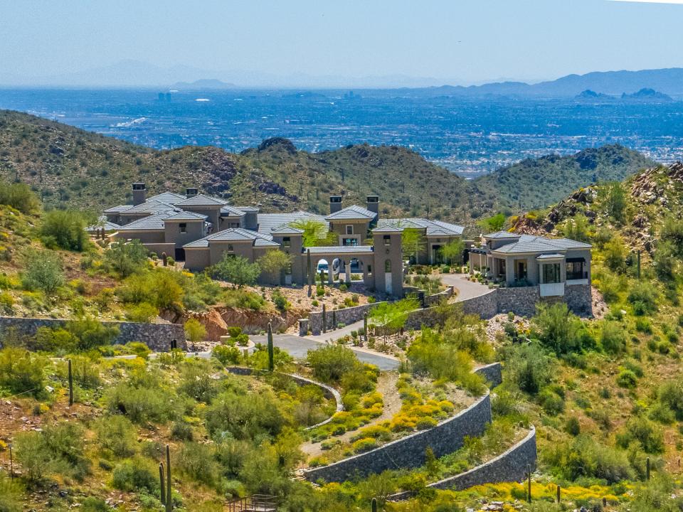 A large gray mansion on a hilltop with mountains in the background