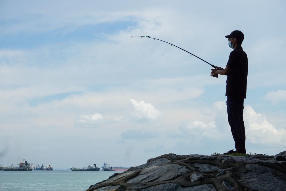 A man fishes from a rock along East Coast Park in Singapore on August 28, 2021. (Photo by Roslan RAHMAN / AFP) (Photo by ROSLAN RAHMAN/AFP via Getty Images)