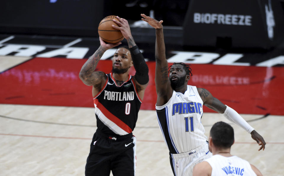 Damian Lillard with the ball in his hands shooting a 3-pointer as James Ennis stretches out his arm in an attempt to block the shot.