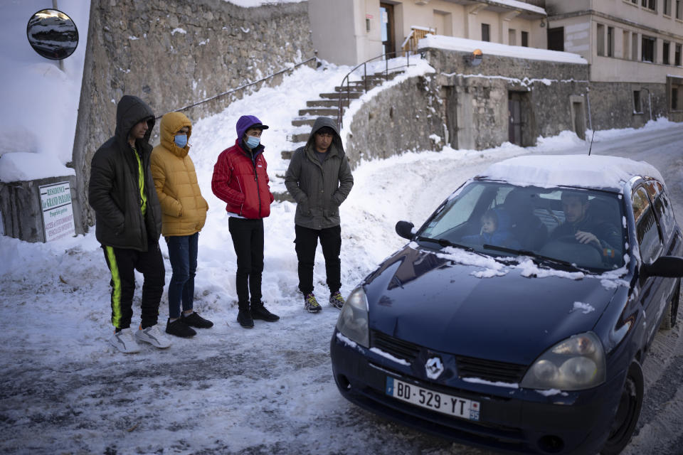 Una familia pasa en auto junto a migrantes afganos que esperan ante un refugio para que los lleven a hacerse una prueba PCR en Briançon, Francia, el sábado 11 de diciembre de 2021. (AP Foto/Daniel Cole)