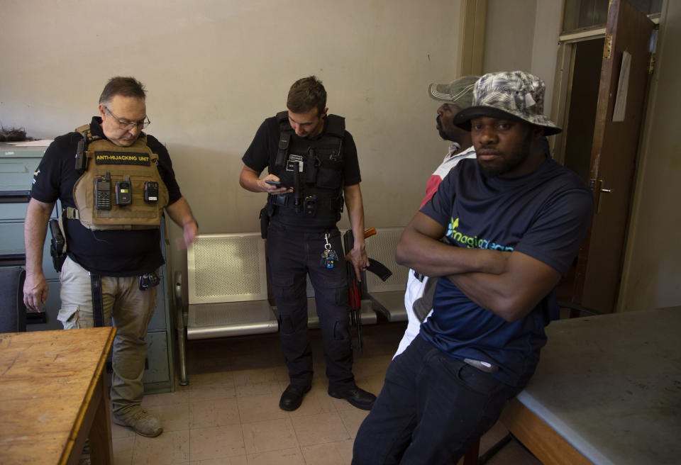 Two men, on right, suspected of driving a stolen vehicle, are handed over to police by private security personal, Anton Koen, left, in a suburb east of Johannesburg, South Africa, Friday, Dec. 1, 2023. Experts have warned that the South African police are losing the battle against crime and that has led those citizens who can afford it, to turn to a booming private security industry. (AP Photo/Denis Farrell)