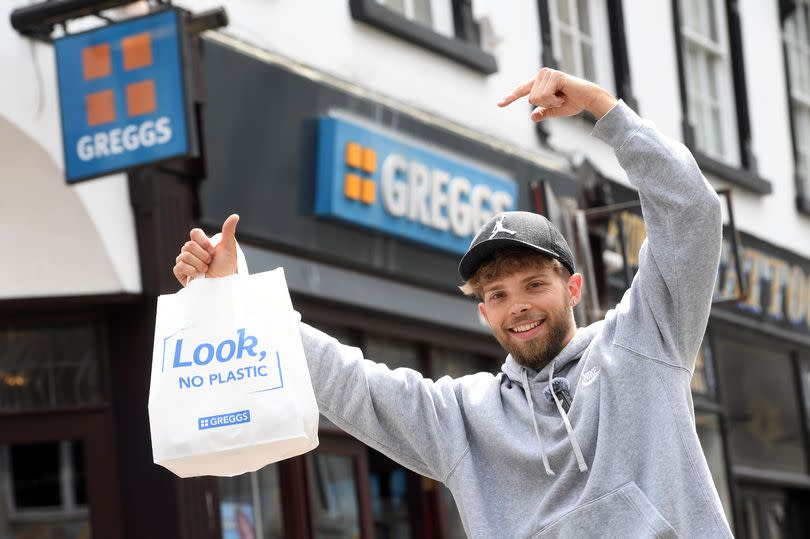 Man holding Greggs bag outside Greggs store.