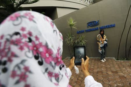 A woman takes pictures of her daughter in front of the Aceh Tsunami Museum in Banda Aceh, December 25, 2014. REUTERS/Beawiharta