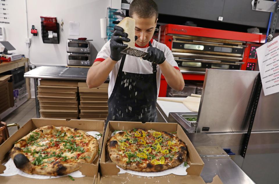 Luis Perez adds a finishing of fresh grated parmesan cheese to a pair of pizzas at the new Peels on Wheels Pizza Garage on Culver Road in Rochester Thursday, July 22, 2021. 