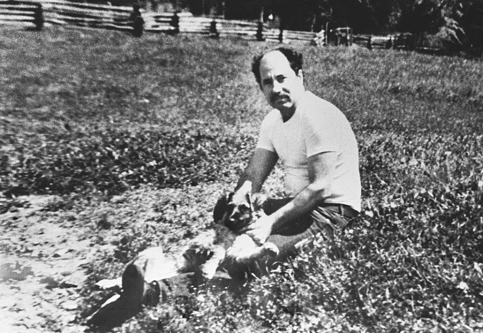 Man sitting on grass, holding small dogs on his lap in an outdoor setting