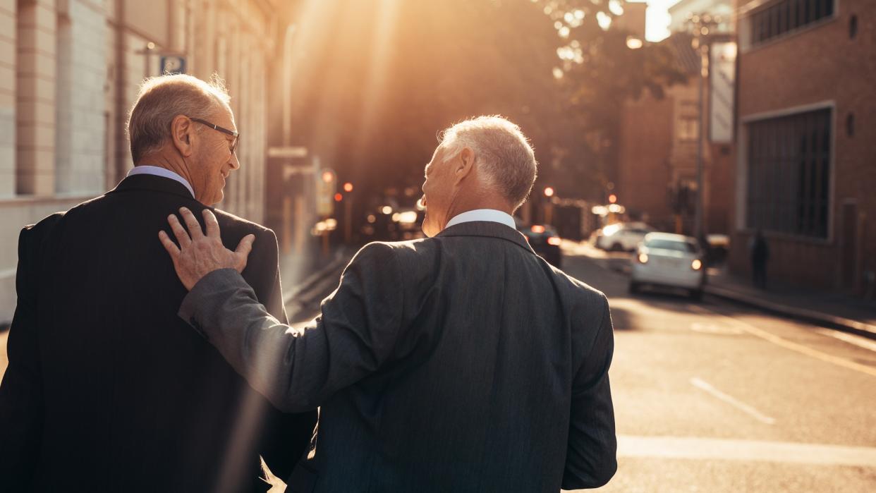 Rear view of two business people walking outdoors and talking next to an office building after a successful business meeting.