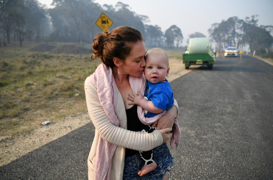 Wytaliba resident Storm Sparks holds her son Zeke Bacon as she waits to get back to her house at a roadblock near Glen Innes, Monday, November 11, 2019. There are more than 60 fires burning around the state, with more than half of those uncontained. (AAP Image/Dan Peled)