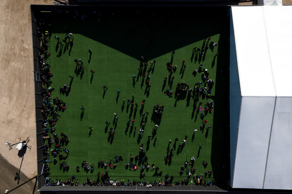 Migrants are seen in a green area outside of a soft-sided detention center after they were taken into custody while trying to sneak into the U.S., Friday, March 19, 2021, in Donna, Texas. (AP Photo/Julio Cortez)