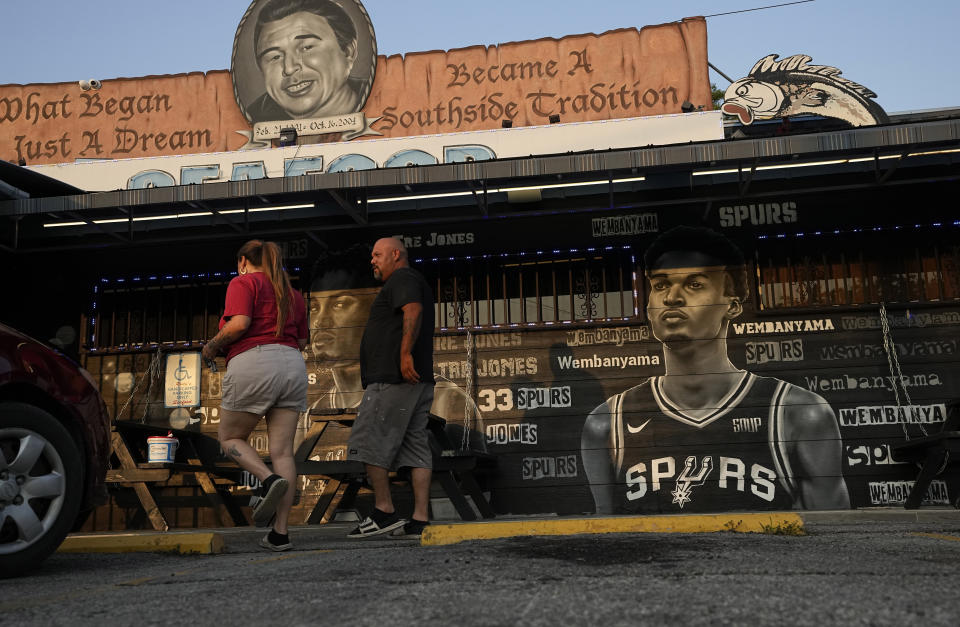 Diners walk past a mural of Victor Wembanyama, a 7-foot-3 French basketball star, that artist Nik Soupe painted as they enter a seafood restaurant in San Antonio, Thursday, June 15, 2023. The San Antonio Spurs are expected to make Wembanyama the No. 1 pick in the NBA draft. (AP Photo/Eric Gay)