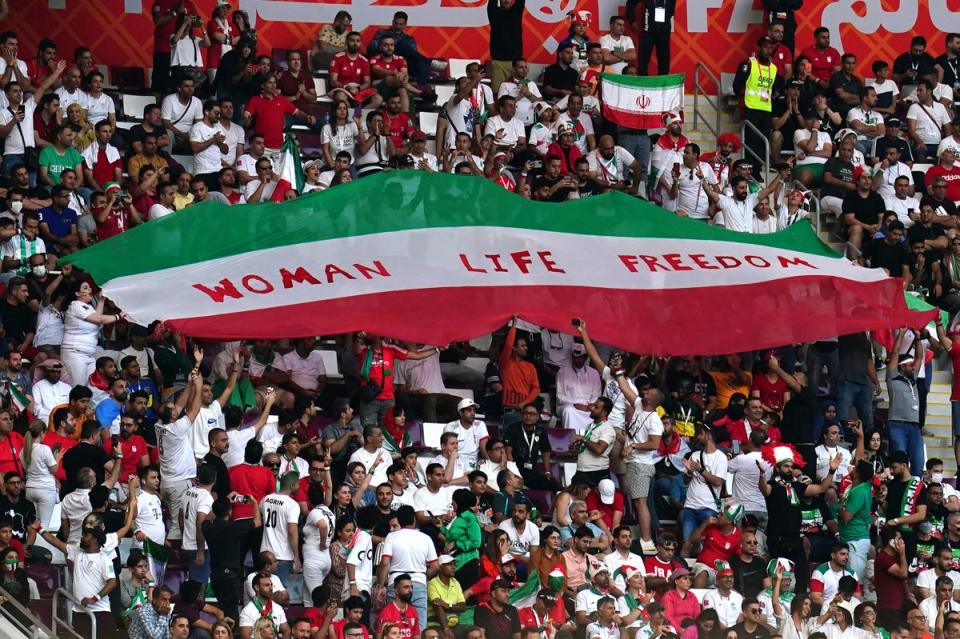 Iran fans in the stands hold up an Iran flag reading 