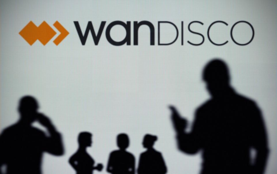 The WANdisco logo is seen on an LED screen in the background while a silhouetted person uses a smartphone - M4OS Photos / Alamy Stock Photo