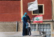 A Lebanese woman with her daughter stands on a rooftop house next to a Lebanese flag and white flag symbolizing the residents' peaceful intentions, as they watch the arrival of an aid supplies convoy, in Tfail village, at the Lebanese-Syrian border, eastern Lebanon, Tuesday April 22, 2014. A Lebanese convoy of soldiers, clerics and Red Cross officials delivered aid Tuesday to a remote village near the Syrian border that was bombed by Syrian government aircraft and blocked by Lebanese militants fighting alongside President Bashar Assad’s forces in the civil war next door. Hezbollah fighters have been patrolling the area on the Lebanese side and fighting has flared up inside Syria, cutting Tfail’s residents off from all sides for months. (AP Photo/Hussein Malla)