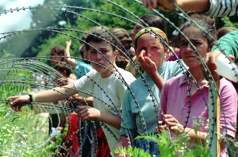 FILE - A July 13, 1995 file photo shows refugees from the overrun U.N. safe haven enclave of Srebrenica looking through the razor-wire at newly arriving refugees, in a UN base 12 kms south of Tuzla, 100kms (60 miles) north of Sarajevo. The Dutch defense minister announced Wednesday that the government will pay veterans of a United Nations peacekeeping mission that failed to prevent the massacre of thousands of Bosnian Muslims by Bosnian Serbs in 1995 5,000 euros each as a "gesture and token of appreciation" for their service in horrific circumstances. (AP Photo/Darko Bandic, File)