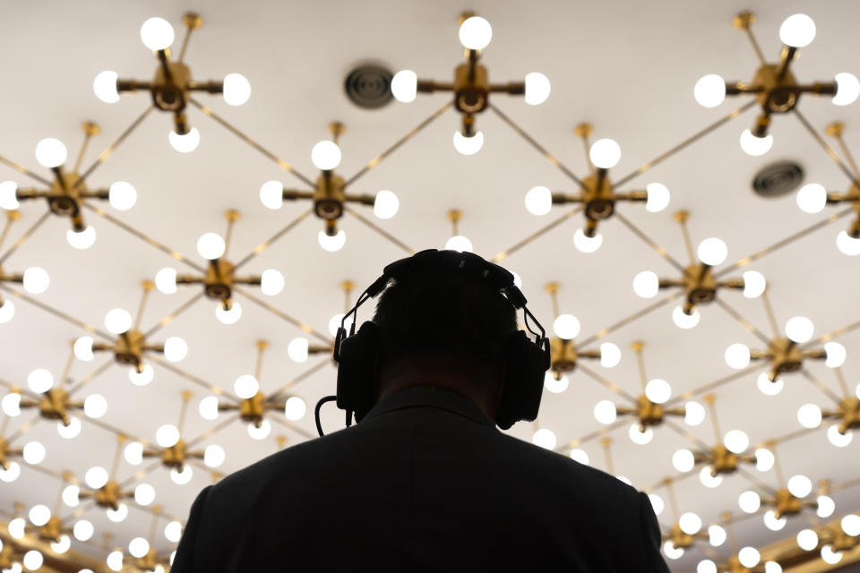 A cameraperson wearing a headset is silhouetted by ceiling lights as he records a remote video press conference by Chinese Foreign Minister Wang Yi held on the sidelines of the annual meeting of China's National People's Congress (NPC) in Beijing, Sunday, March 7, 2021. (AP Photo/Mark Schiefelbein)