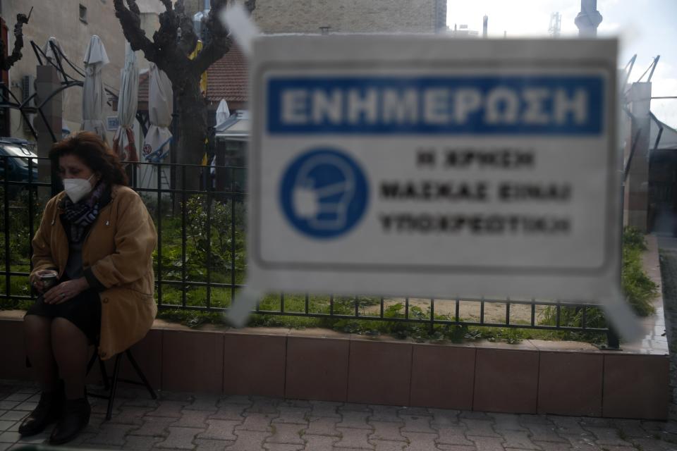 A woman sits as a sign reads "For your information, the use of mask is mandatory" in Athens, Wednesday, March 3, 2021. Greece has recorded a new spike in COVID-19 infections, nearly half of which were recorded in the greater Athens region where hospital intensive care units are quickly filling up. (AP Photo/Thanassis Stavrakis)