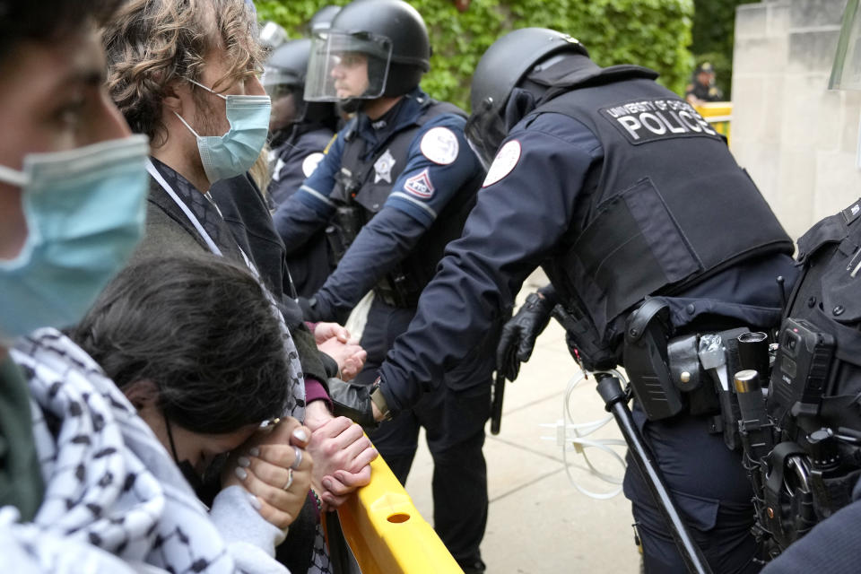 A pro-Palestinian protester rests her head on her clasped hands while she stands before University of Chicago police officers while officers kept protesters from the university's quad while the student encampment is dismantled Tuesday, May 7, 2024, in Chicago. (AP Photo/Charles Rex Arbogast)