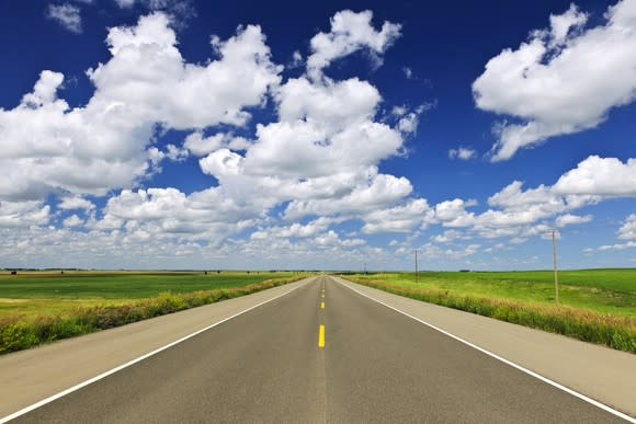 An open road and sky with puffy clouds