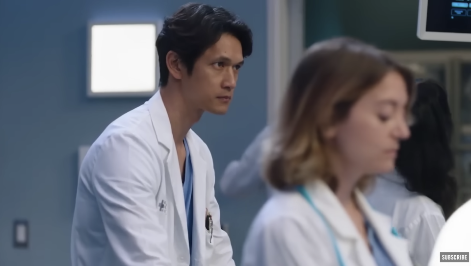 Harry Shum Jr. on the set of Grey's Anatomy wearing scrubs and a lab coat