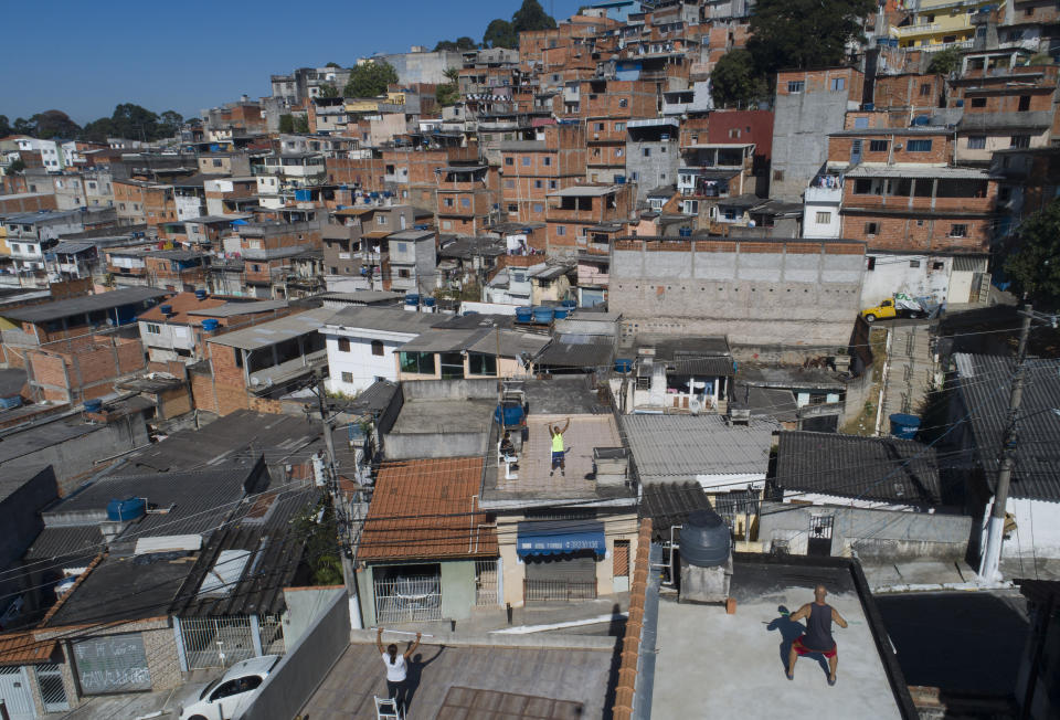 Physical trainer Ivan Nascimento, center, gives an outdoor workout class to neighbors from the roof of his home during a quarantine imposed by the state government to help contain the spread of the new coronavirus, in the Brasilandia neighborhood of Sao Paulo, Brazil, Sunday, May 17, 2020. (AP Photo/Andre Penner)