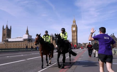 A runner waves to two mounted police officers on Westminster Bridge, following the attack in Westminster earlier in the week, in London, Britain March 25, 2017. REUTERS/Peter Nicholls
