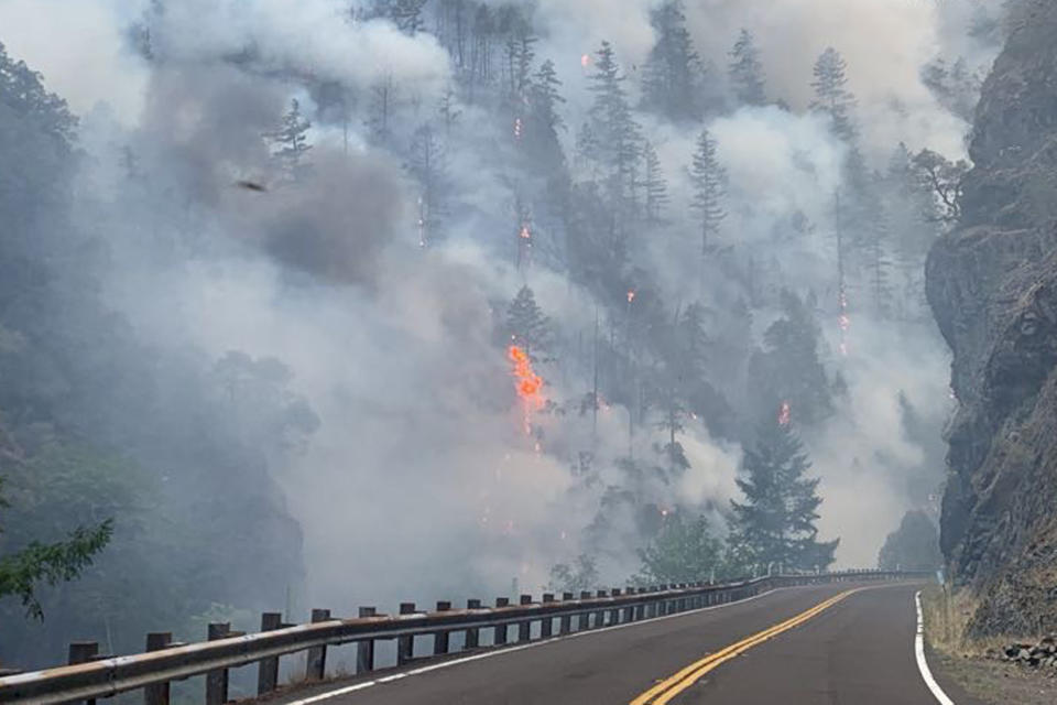 In this photo provided by Caltrans, smoke and flames rise from the Smith River Complex Fire next to the closed U.S. Route 199 in Gasquet, Calif., on Wednesday, Aug. 16, 2023. (Caltrans via AP)