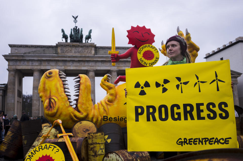 A Greenpeace activist poses with a poster in front of a mock-up dinosaur in front of the Brandenburg Gate during a rally marking the nuclear shutdown in Germany in Berlin, Germany, Saturday, April 15, 2023. Germany is shutting down its last three nuclear power plants on Saturday, April 15, 2023, as part of an energy transition agreed by successive governments. The signs read: 'Nuclear Power No Thanks' and the words on the dinosaur: 'German nuclear power defeated on April 15, 2023'. (AP Photo/Markus Schreiber)