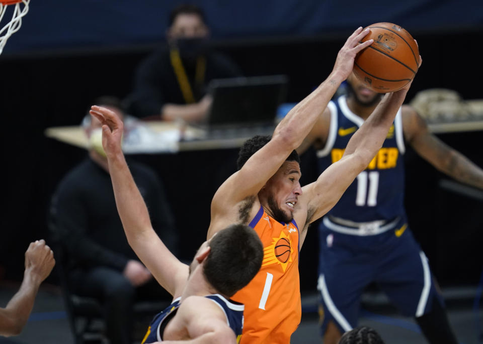 Phoenix Suns guard Devin Booker pulls in a rebound as Denver Nuggets center Nikola Jokic defends during the second half of an NBA basketball game Friday, Jan. 1, 2021, in Denver. The Suns won 106-103. (AP Photo/David Zalubowski)