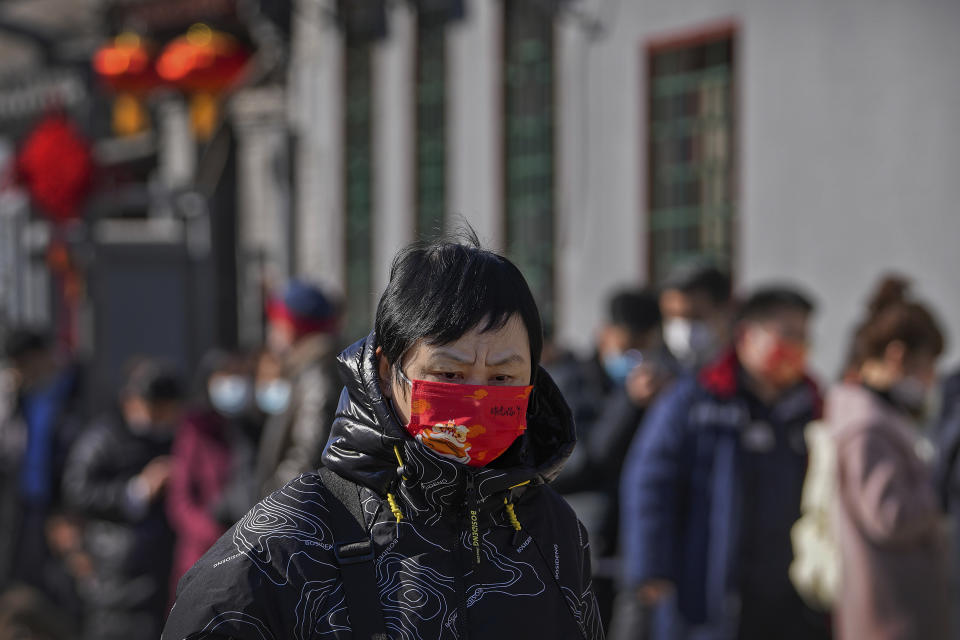 A woman wearing a face mask to help protect from the coronavirus walks by masked residents line up outside a COVID-19 test site in Beijing, Tuesday, Feb. 8, 2022. China has ordered inhabitants of the southern city of Baise to stay home and suspended transportation links amid a surge in COVID-19 cases at least partly linked to the omicron variant. (AP Photo/Andy Wong)