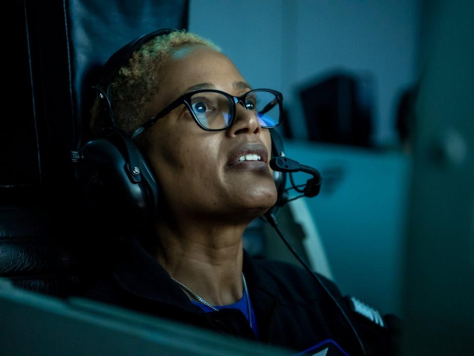 sian proctor wearing a headset looking at a screen in dark blue room