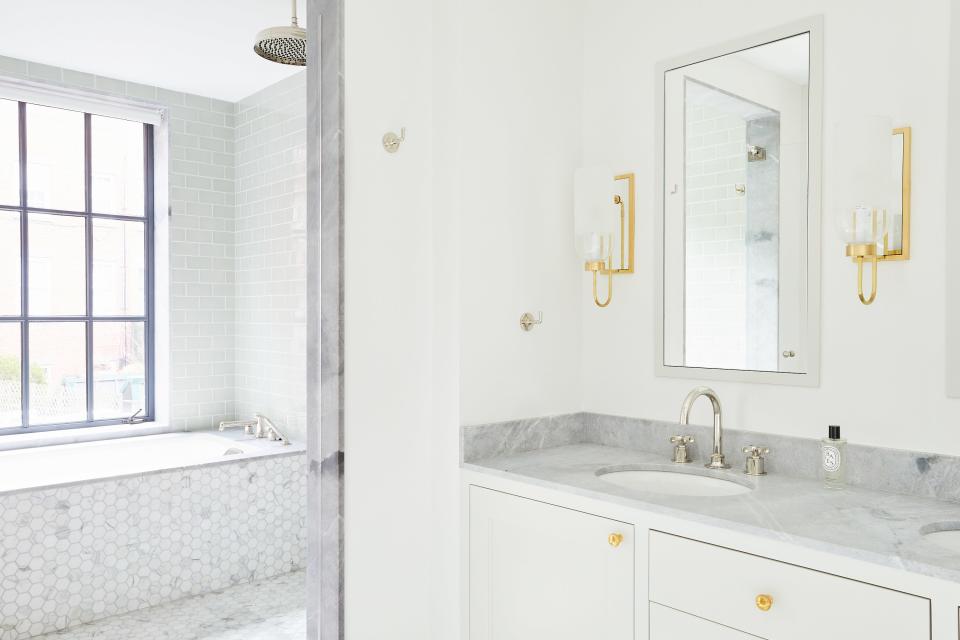 The main bath is equally serene thanks to a subtle white-and-gray color palette. The sconces are by Urban Electric Company, and the hardware is by E.R. Butler & Co.