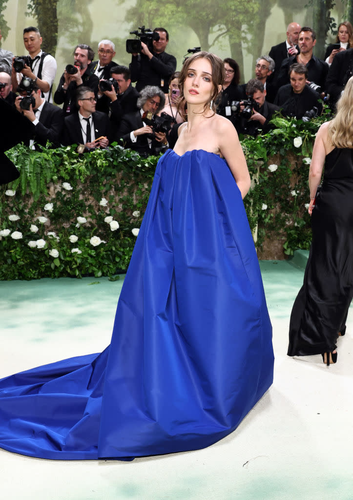 Talia in a voluminous strapless gown with a flowing train, standing before photographers