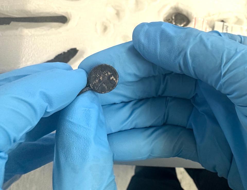 blue gloved hands hold a small ancient blackened pendant with a thick cross engraved on it