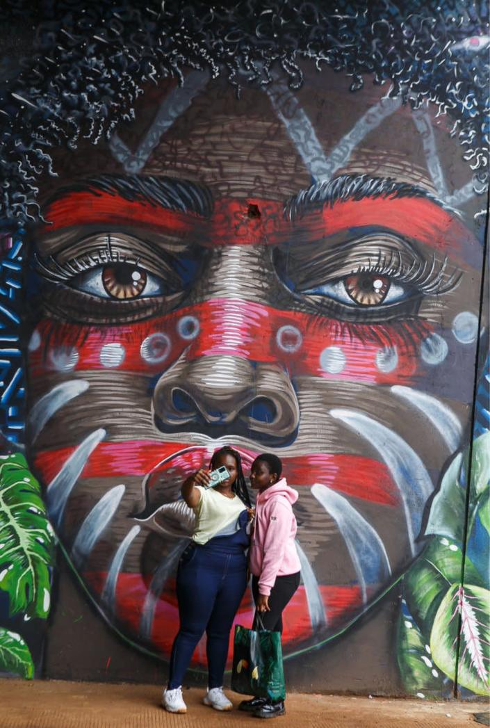 Two Kenyan women take selfies next to the murals on display at the Kenya Defence Forces Air Show at the Uhuru Gardens National Monument and Museum. The free Air Show was a forerunner of commissioning the Uhuru Gardens National Monument and Museum. It was led by Kenya Air Force and included the Kenya wildlife services and civilian aerobatic and sky diving teams. The aim was to entertain and educate the public.