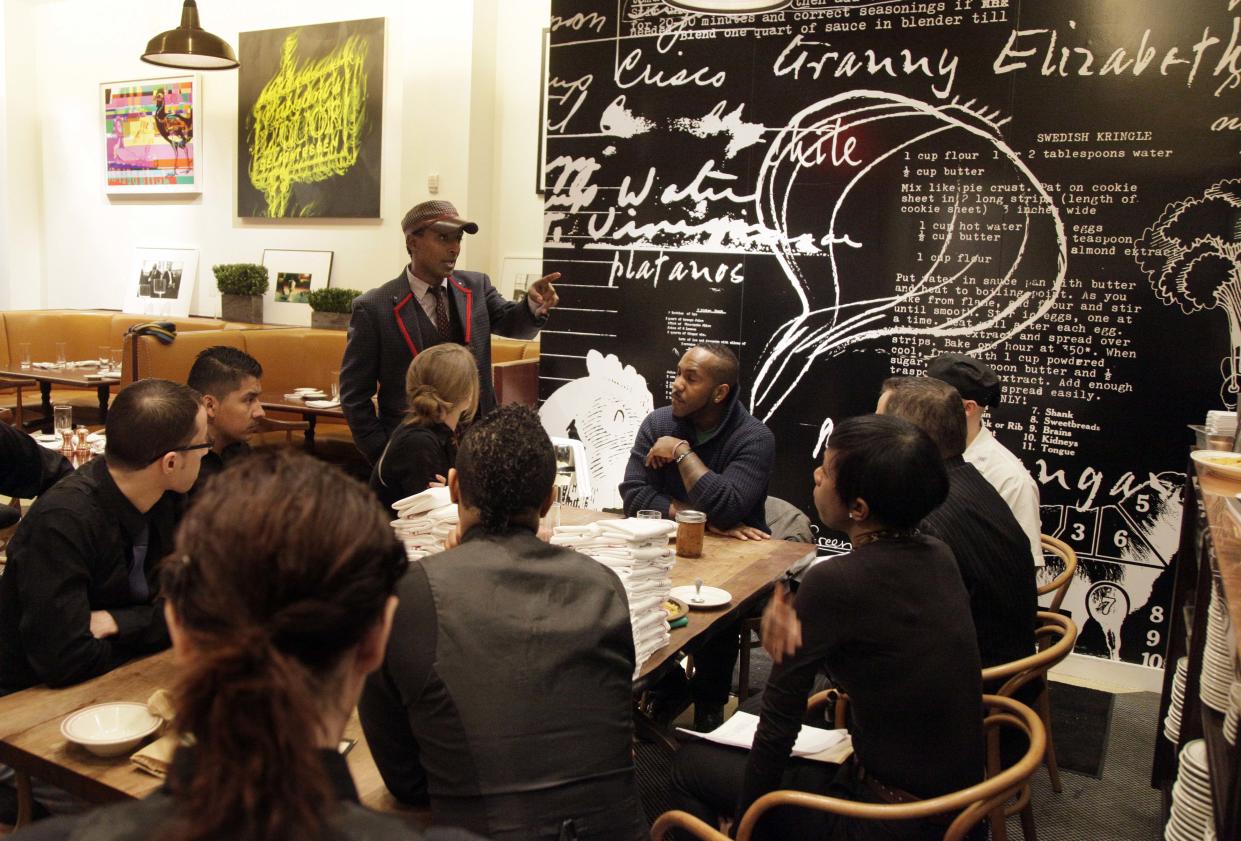 In this Feb. 7, 2012 photo, chef Marcus Samuelsson, owner of the Red Rooster, standing, talks with his staff at his restaurant in New York. Born in Ethiopia, raised in Sweden, Samuelsson's ambitious Harlem eatery pulsates with action any day of the week. Not merely a restaurant, Red Rooster aims to be the hub of a revitalized Harlem.  (AP Photo/Richard Drew)