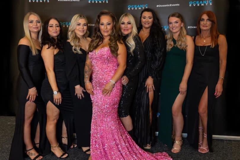 Jade wearing a bright pink, sparkly dress pictured with seven other women wearing black dresses