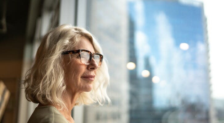 Image shows a woman looking out a window. T. Rowe Price says investors should expect returns in the coming period to be lower than recent years.