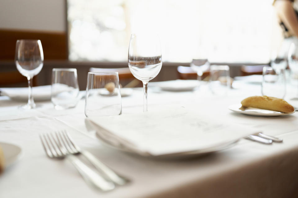 Elegant table setting for a formal meal with clean plates, wine glasses, and cutlery on a white linen tablecloth