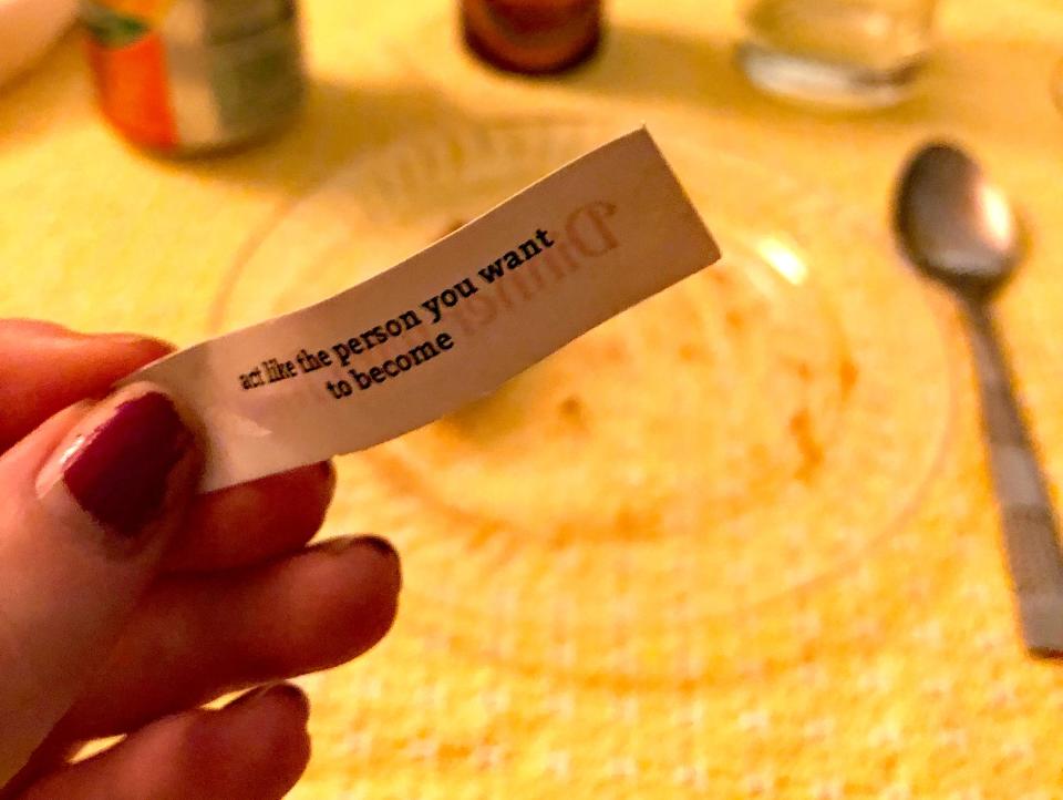 hand holding up fortune cookie fortune in front of a dinner table at dinner with friends dinner party