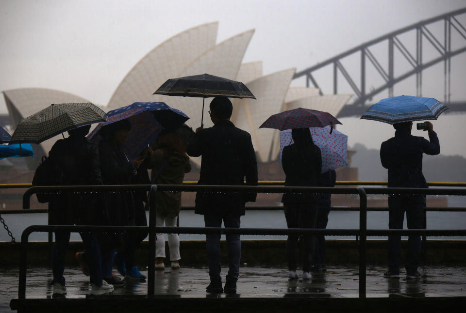 Tourists hold umbrellas as they take photographs of the Sydney Opera House and Sydney Harbour Bridge from Mrs Macquarie's Chair on a rainy day in Sydney.