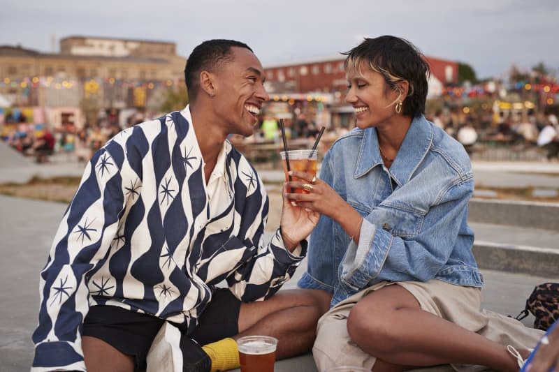 Happy heterosexual couple holding drink glass together while sitting on promenade during weekend