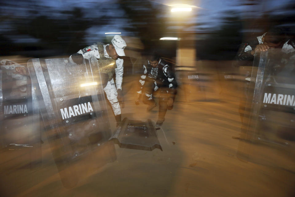 Mexican National Guards pick up their shields after they fell by accident when a journalist's backpack hit them by mistake, on the Mexican side of the Suchiate River near Ciudad Hidalgo, Mexico, before sunrise Wednesday, Jan. 22, 2020, on the border with Guatemala. The number of migrants stuck at the Guatemala-Mexico border continued to dwindle Wednesday as detentions and resignation ate away at what remained of the latest caravan. (AP Photo/Marco Ugarte)